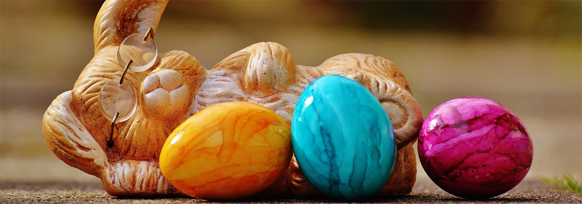 Ein liegender Osterhase mit drei gefärbten Eiern vor sich